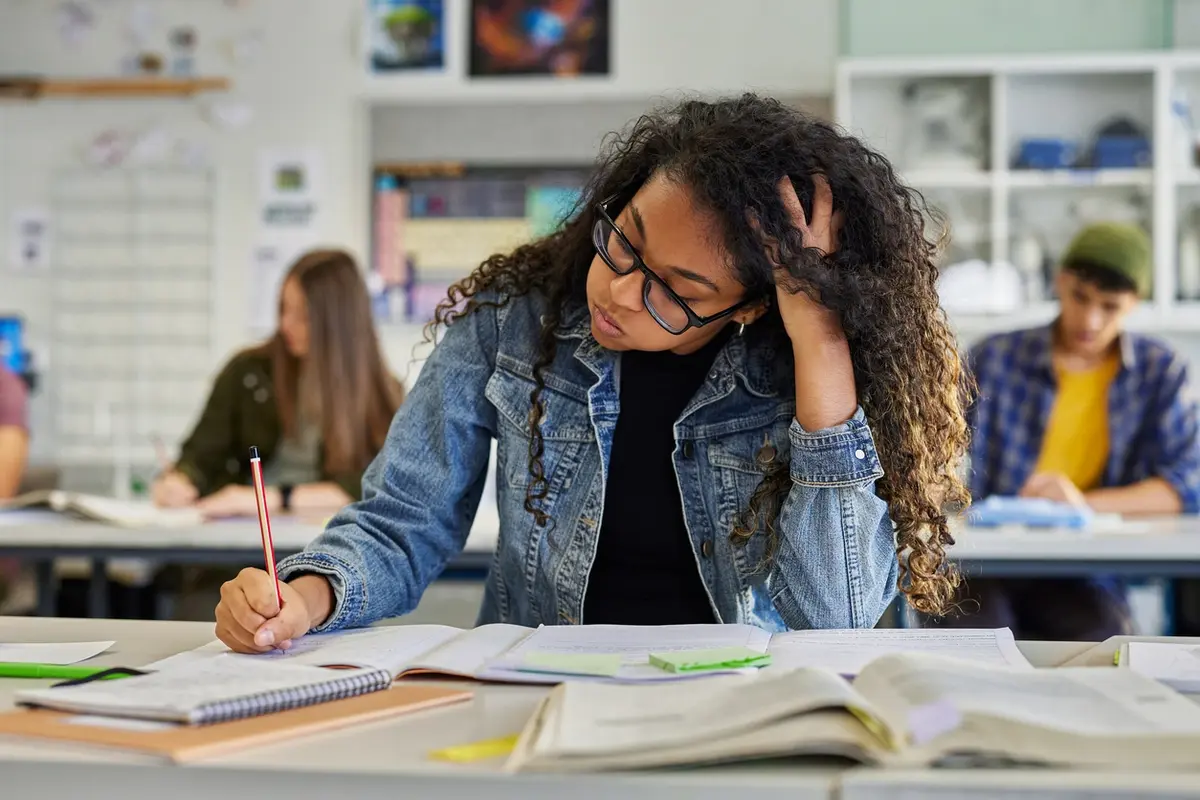 A tired student resting her head while studying, showing signs of academic burnout from prolonged homework pressure.